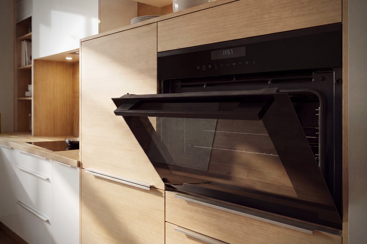 Four encastrable avec porte ouverte dans une cuisine moderne avec façades en bois et éléments blancs.