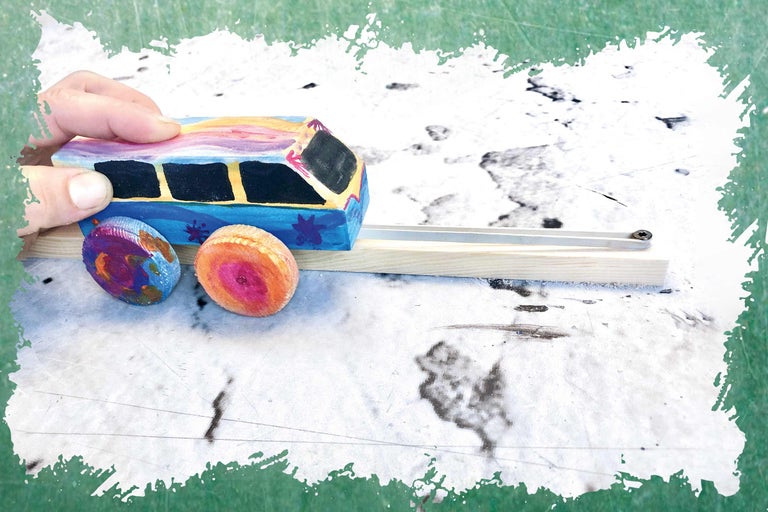 Une main pousse une voiture jouet en bois peinte de couleurs vives sur une piste en bois.