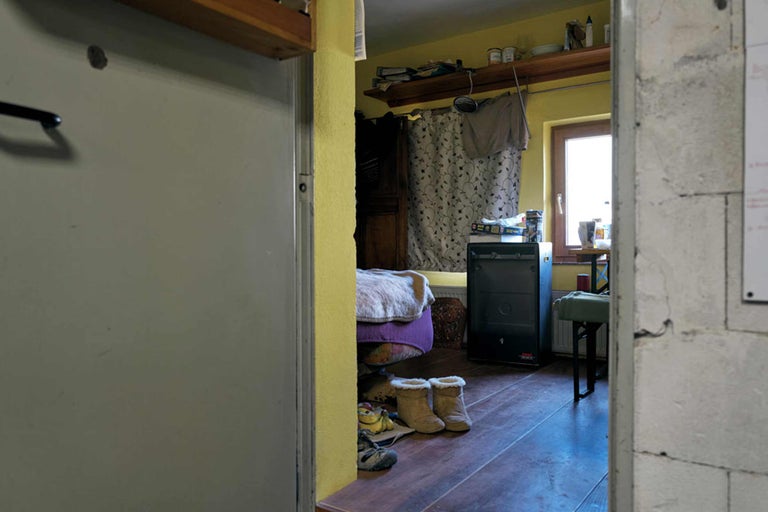 Blick durch eine offene Tür in einen Wohnraum mit Holzofen und Schuhen auf dem Boden