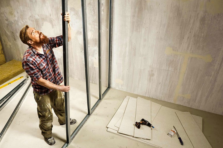 Mann montiert Trockenbauwand im Innenraum mit Werkzeugen und Materialien