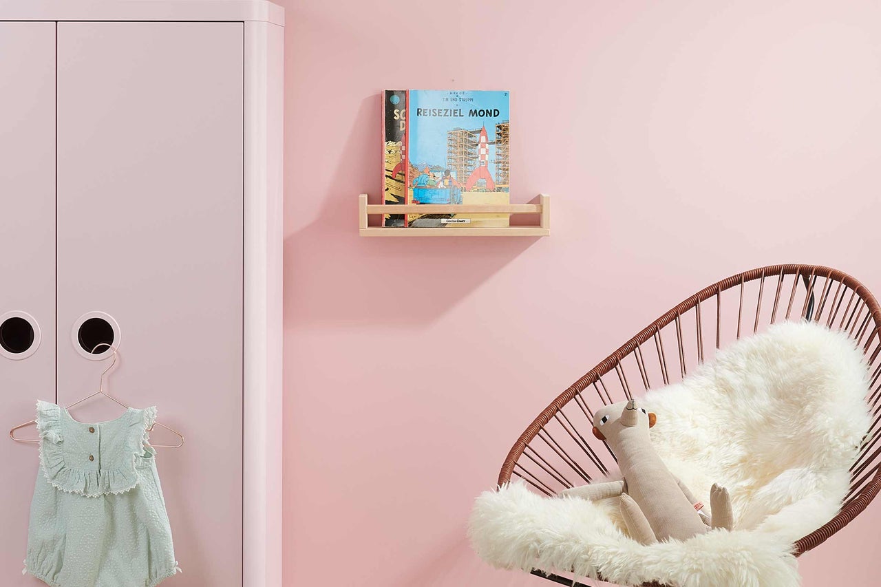 Kinderzimmer mit Garderobe, Bücherregal mit Büchern und Sessel mit Kissen und Stofftier