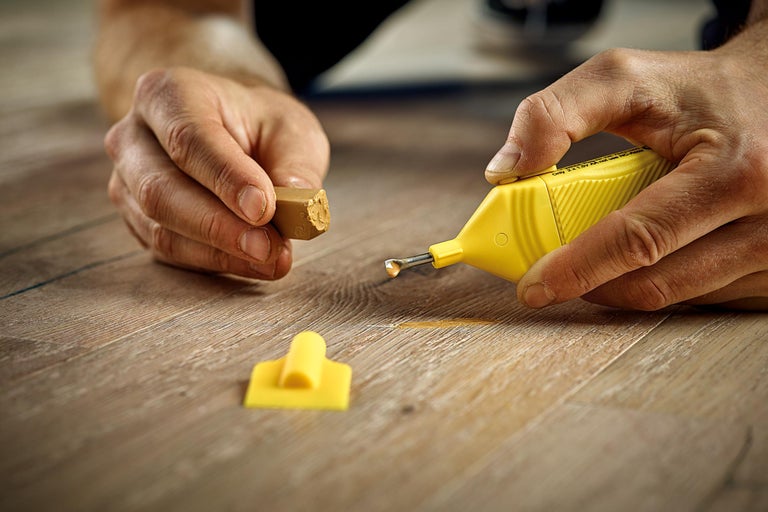 Kit de réparation pour stratifié et bois avec mastic et appareil de fusion utilisé sur un plancher en bois