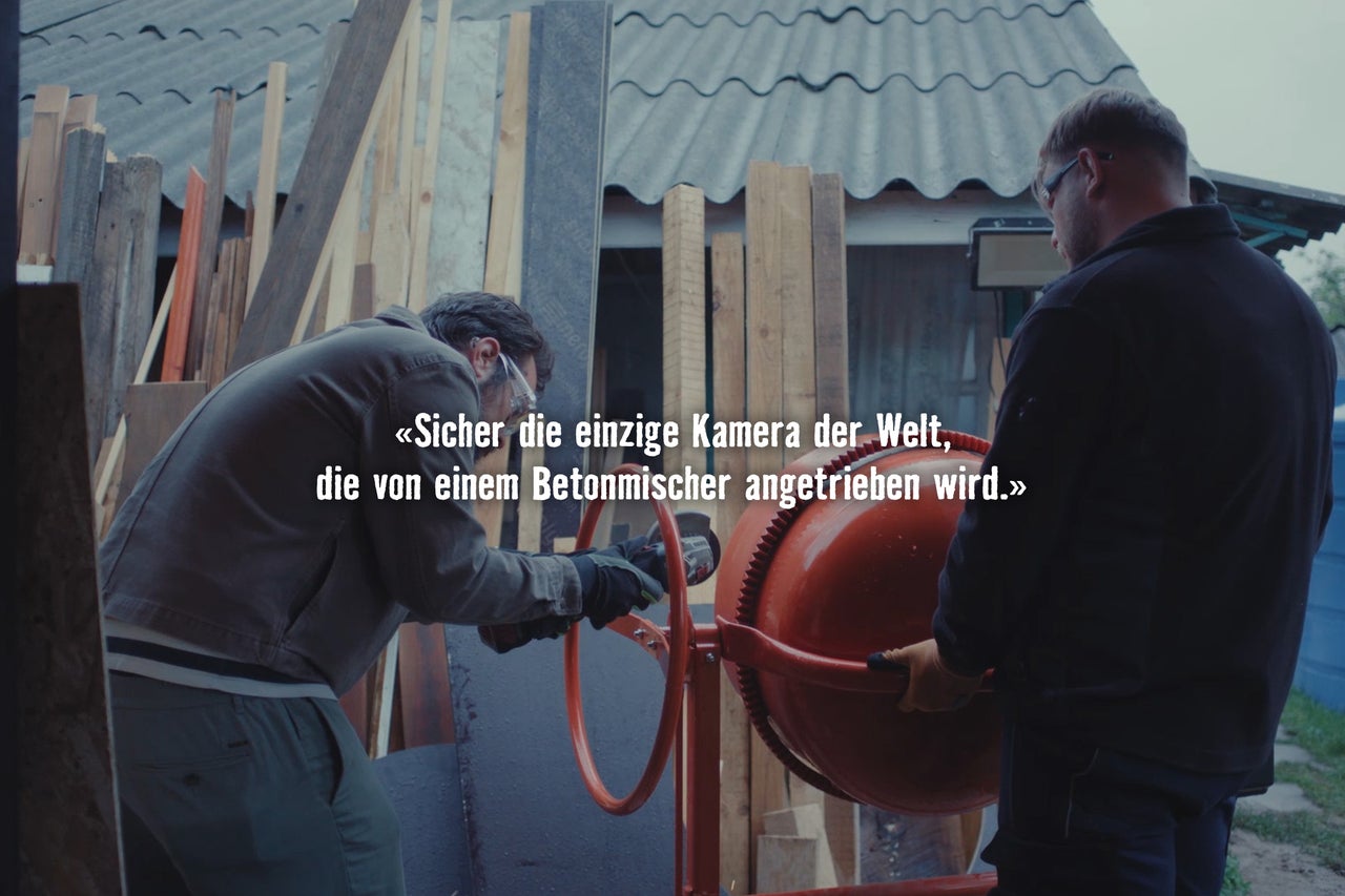 Zwei Handwerker nutzen einen Betonmischer auf einer Baustelle mit gelagerten Holzlatten im Hintergrund.