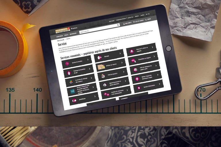 Tablette affichant la page de services Hornbach, entourée d'outils et de notes évoquant une ambiance de bricolage.