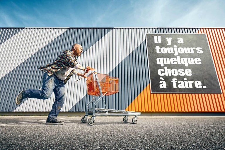 Homme courant avec un caddie devant un panneau publicitaire Hornbach