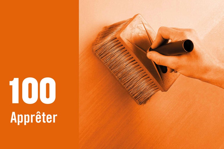 Une main applique une couche d'apprêt sur un mur à l'aide d'une brosse