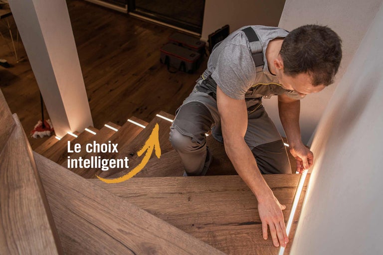 Artisan installant des bandes LED sur un escalier en bois pour l'éclairage de l'escalier