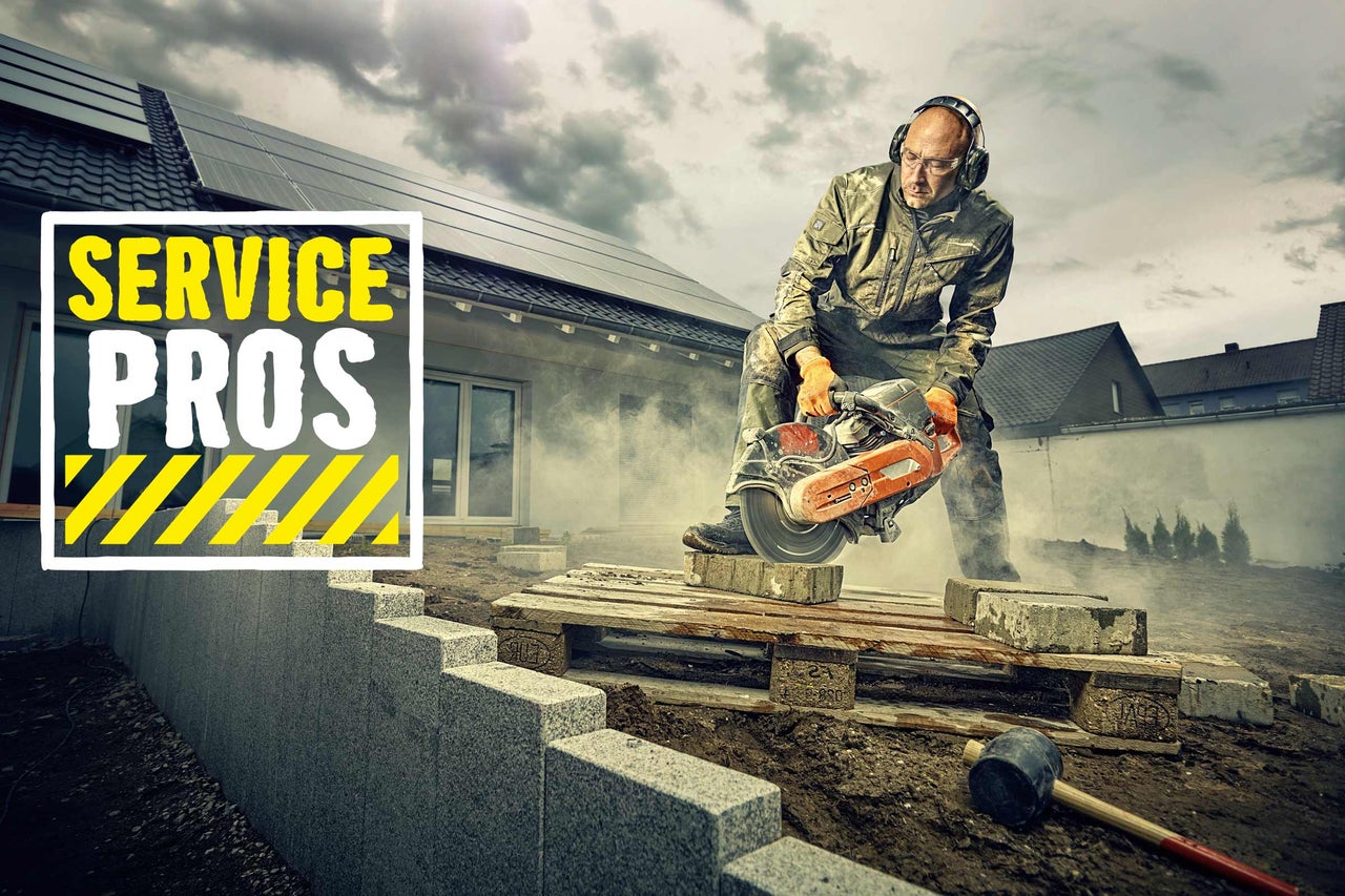 Un artisan coupe de la pierre avec une scie à pierre à l'extérieur. Logo Service Pros.