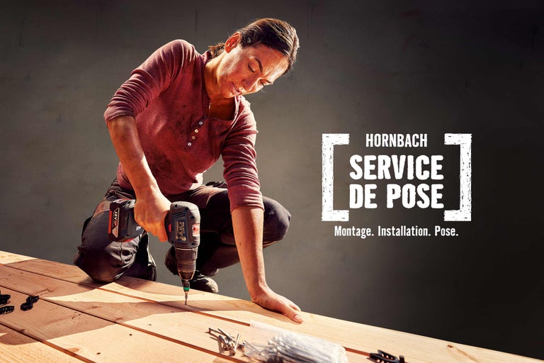 Une femme travaille avec une perceuse sur une terrasse en bois dans le cadre du service de montage Hornbach