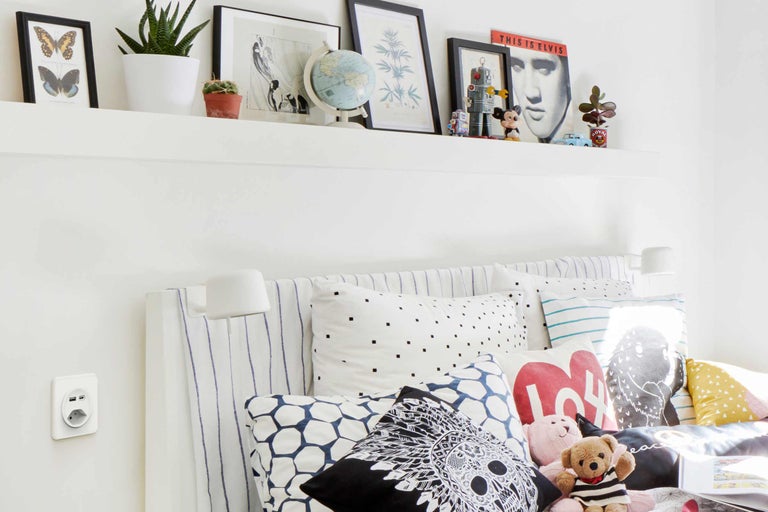 Chambre claire avec lit, coussins, étagère murale et décoration