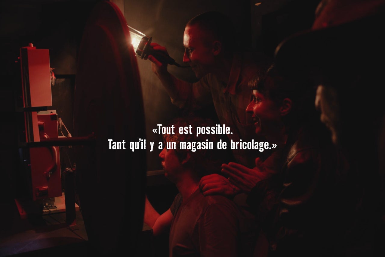 Trois personnes travaillent de manière concentrée sur un projet technique avec des outils dans une pièce faiblement éclairée.