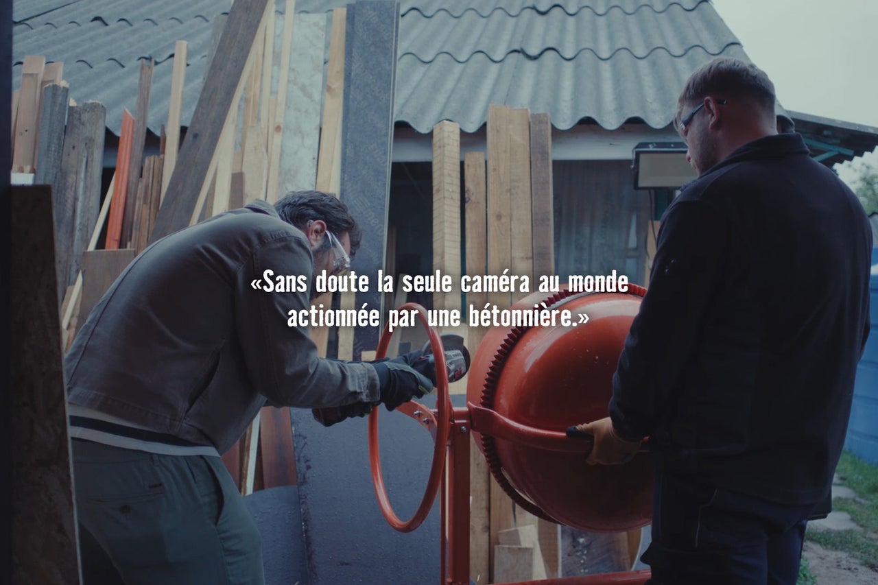 Deux artisans travaillent dans un atelier avec une bétonnière et une meuleuse d angle devant des lattes de bois empilées.