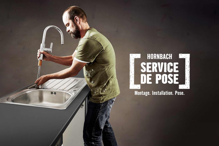 Un homme installe un robinet dans un évier, avec le logo Hornbach Service de Pose en arrière-plan.