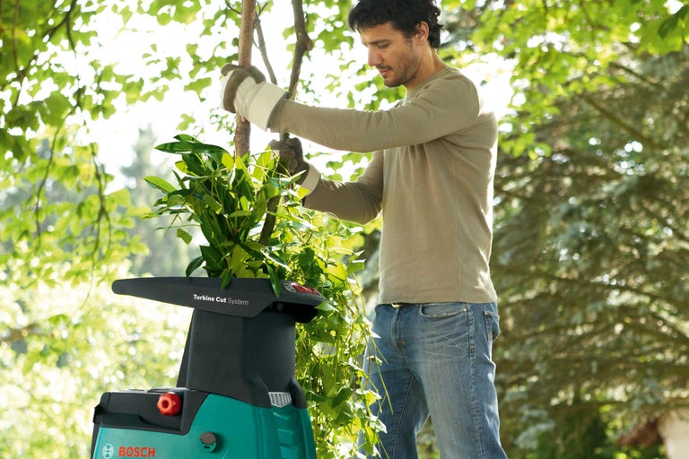 Un homme utilise un broyeur de jardin avec des déchets verts, avec des arbres en arrière-plan