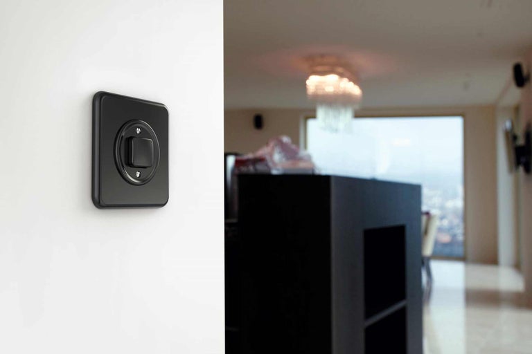 Un interrupteur noir sur un mur, qui montre un salon moderne.