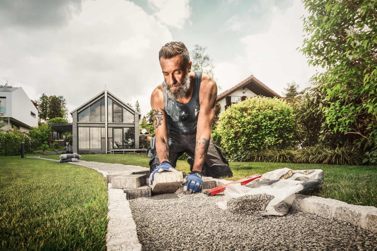 Mann verlegt Pflastersteine im Gartenweg mit Haus im Hintergrund