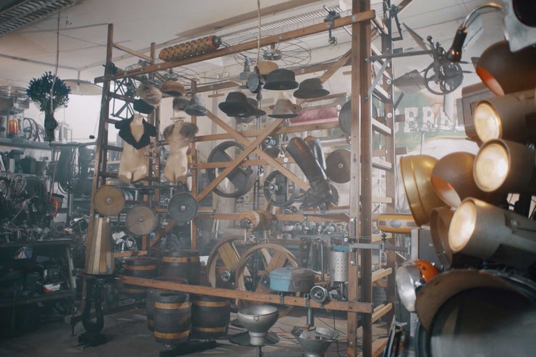 Scène avec chapeaux, vêtements, barils, roues et phares sur une structure en bois dans une pièce.