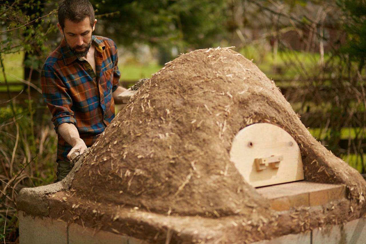 Un homme construit un four en argile dans le jardin.