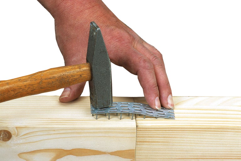 Ein Hammer schlägt eine Nagelplatte in zwei Holzstücke.