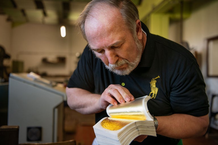 Un homme manipule de la feuille d'or dans un livre.