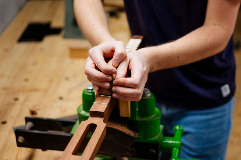 Personne travaillant sur un manche de guitare dans un étau