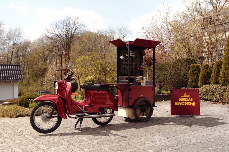Cyclomoteur rouge avec stand de vente de nachos sur des pavés