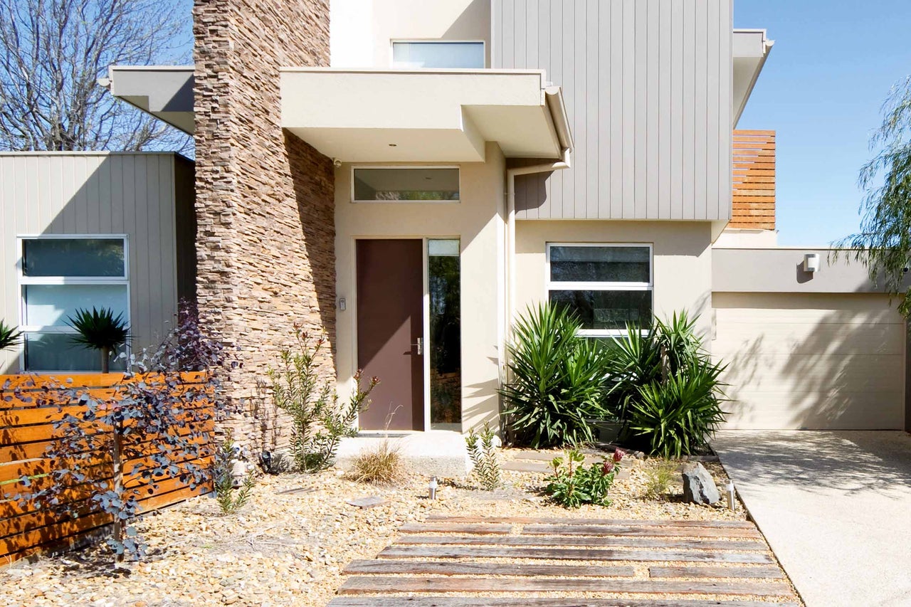 Extérieur d'une maison moderne avec façade en pierre, clôture en bois et aménagement paysager