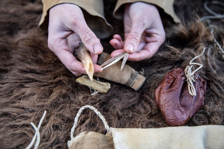 Nahaufnahme von Händen, die ein Ahlen-Werkzeug mit Zubehör über einem Fell halten