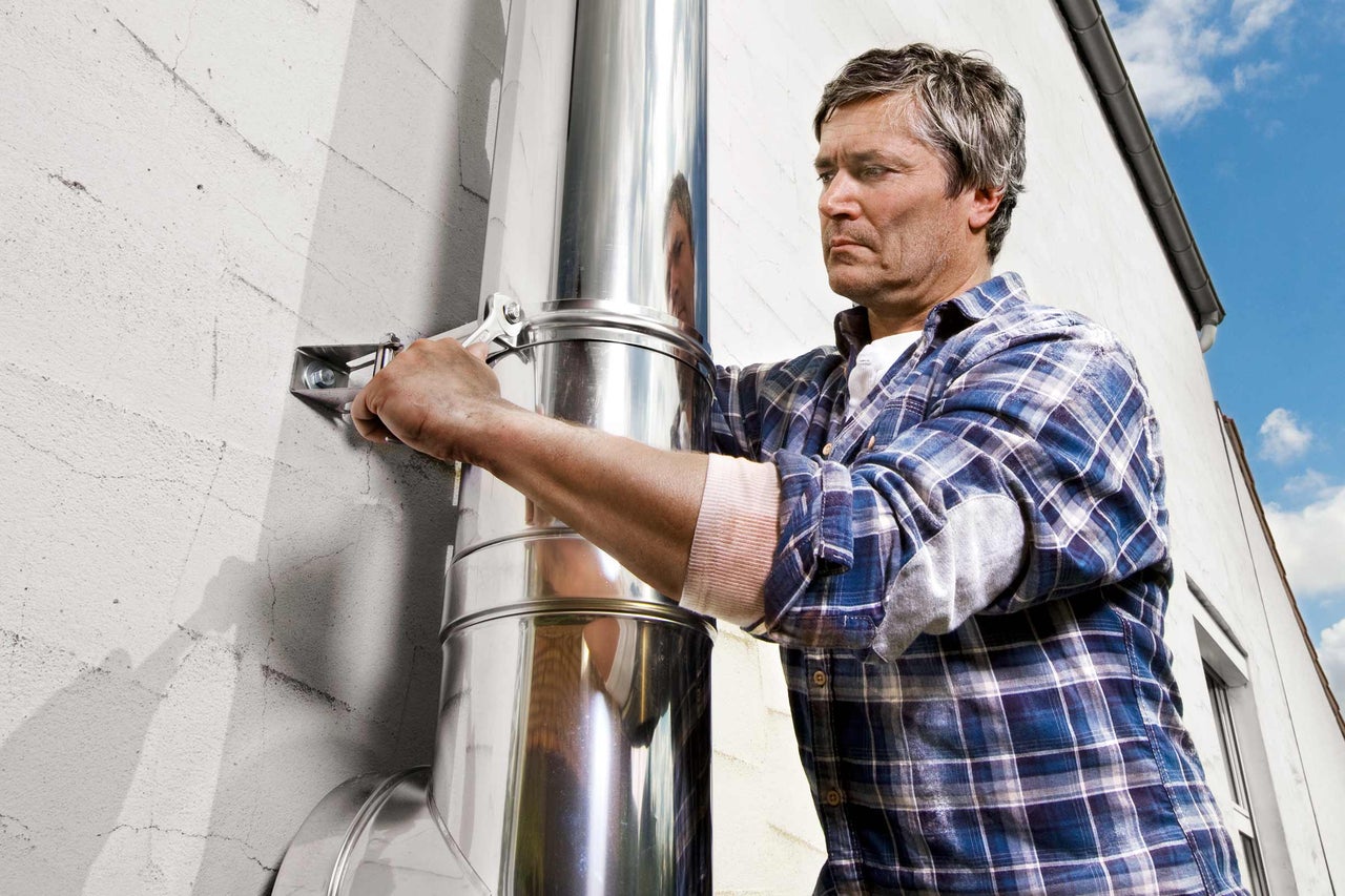 Un homme monte un conduit de cheminée en acier inoxydable à l'aide d'une clé sur un mur de maison.