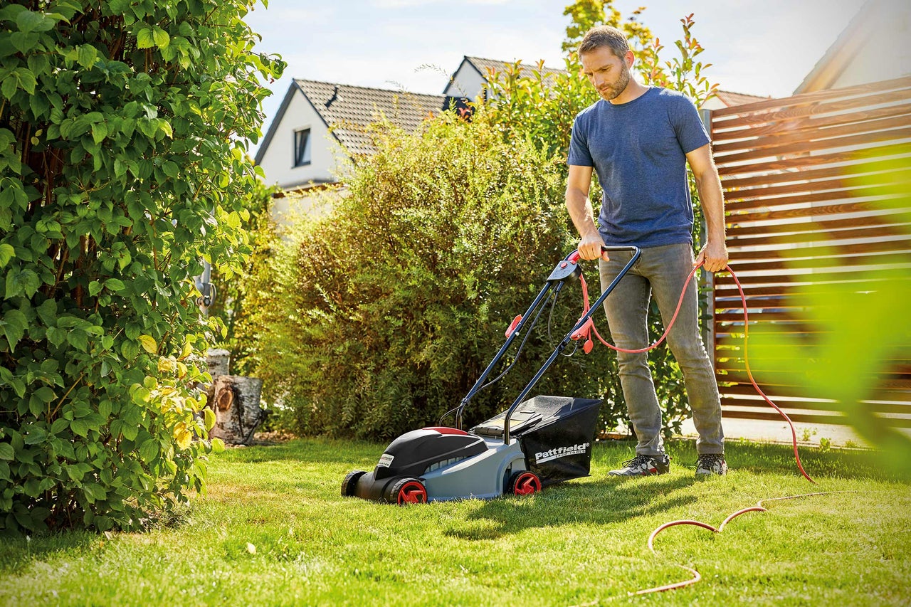 Un homme tond la pelouse avec une tondeuse à gazon électrique dans le jardin.