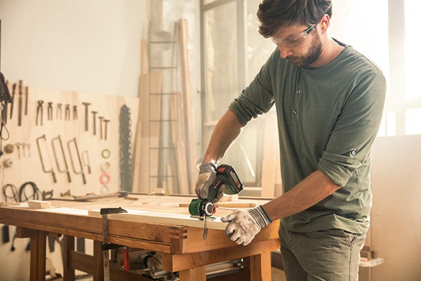 Handwerker bei der Arbeit mit einem Multifunktionswerkzeug an einem Werkstück in einer Werkstatt.