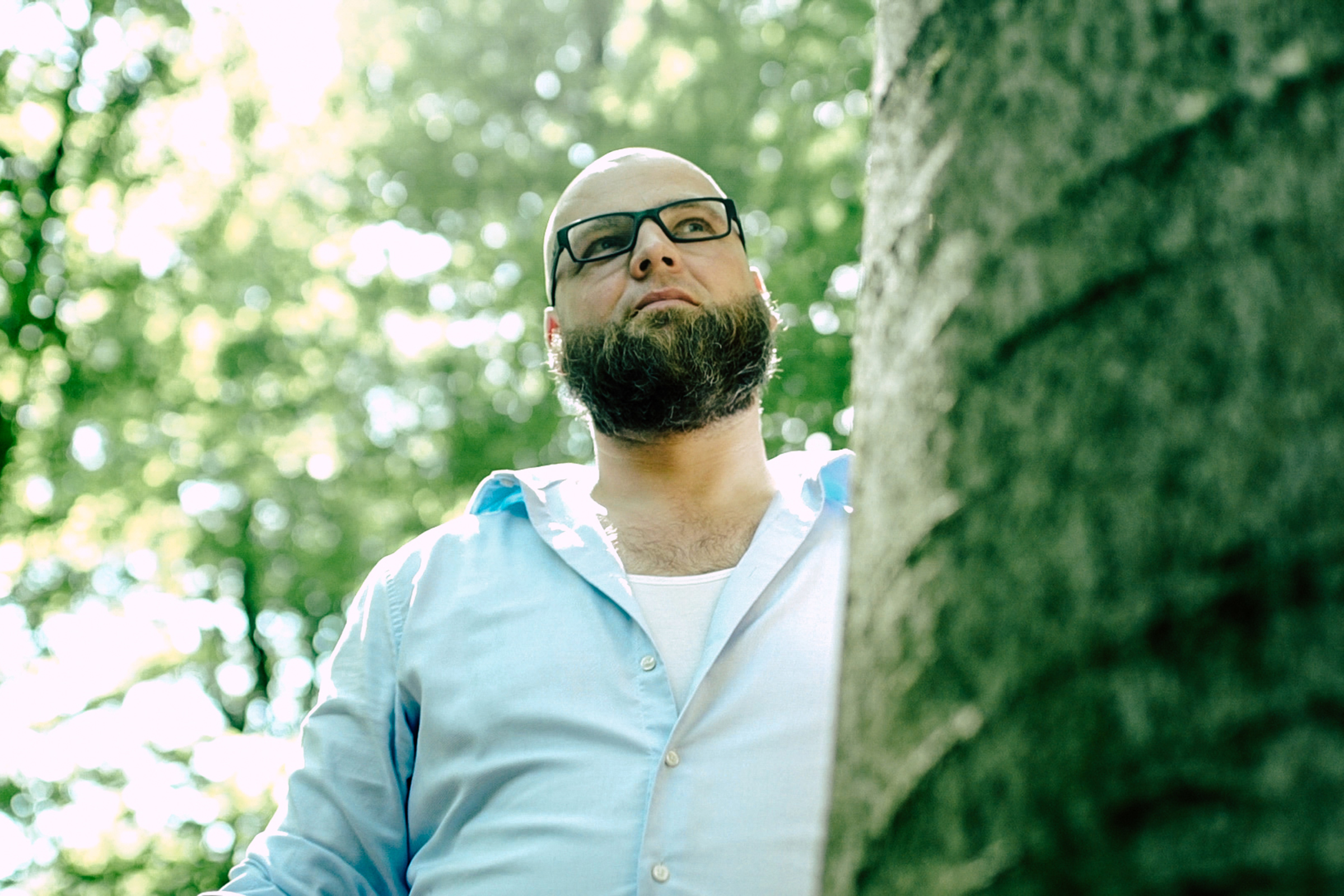 Homme à lunettes se tient à côté d'un arbre