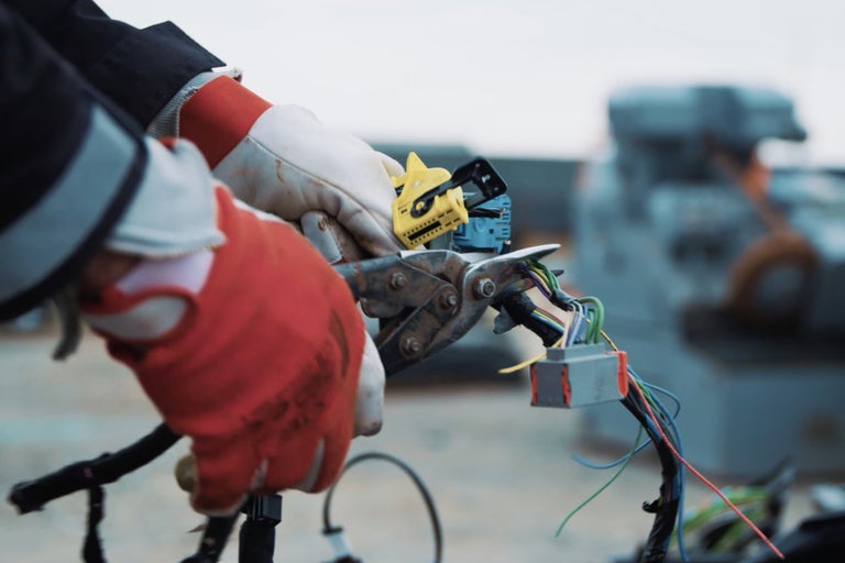 Un électricien portant des gants de travail coupe des câbles avec une pince.