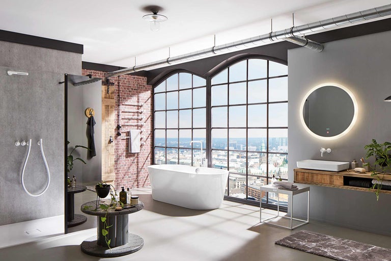 Salle de bains de style loft avec baignoire, douche et lavabo devant une grande fenêtre avec vue sur la ville