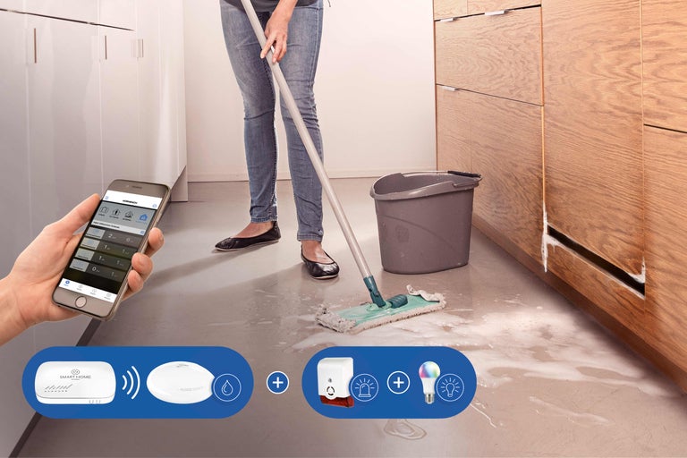 Femme nettoie de l'eau dans la cuisine, contrôlée avec un smartphone et le système Smart Home de Hornbach