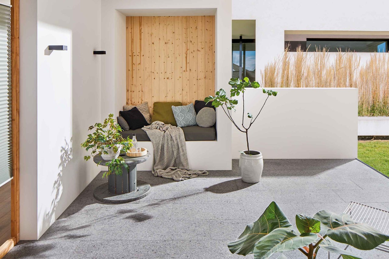 Modern gestalteter Aussenbereich mit Sitzbereich, Pflanzen und Bodenplatten.