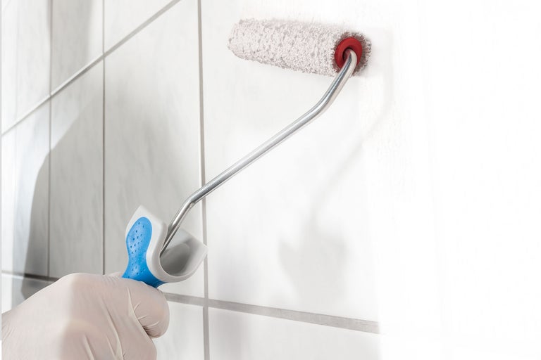 Une personne gantée utilise un rouleau à peinture pour peindre un mur.