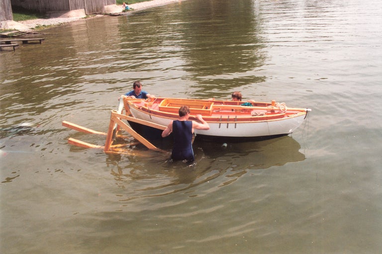 Personen lassen ein hölzernes Ruderboot zu Wasser.