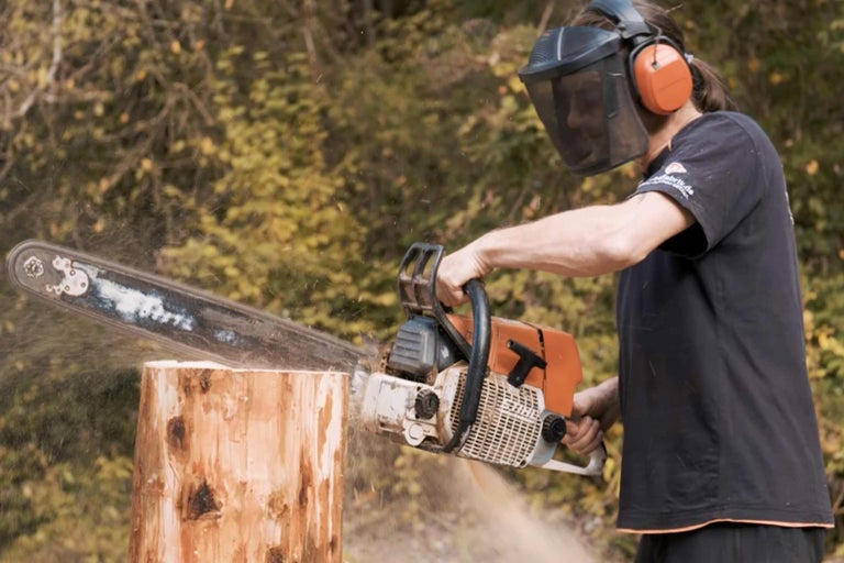 Mann mit Schutzausrüstung sägt mit einer Kettensäge Holz