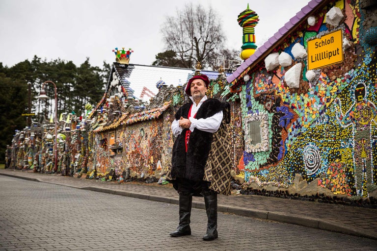 Homme en costume devant le château Lilliput, décoré de mosaïques et d'éléments décoratifs
