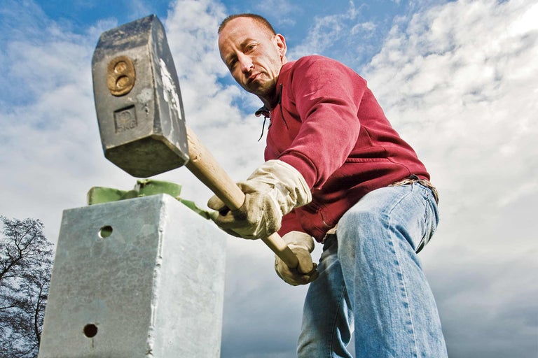 Mann mit Fäustel beim Einschlagen eines Metallpfostens