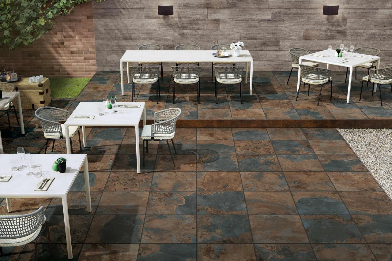 Terrasse mit Bodenfliesen, Tischen und Stühlen im Aussenbereich.