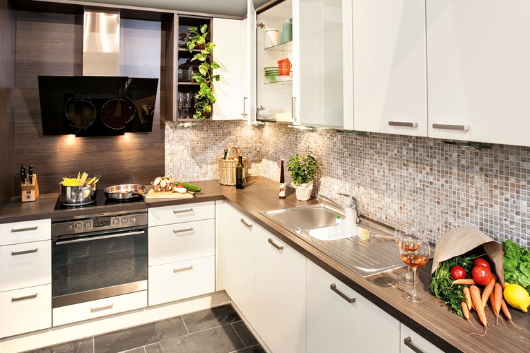 Küchenansicht mit Spüle, Kochfeld, Backofen, Dunstabzugshaube und Küchenutensilien.