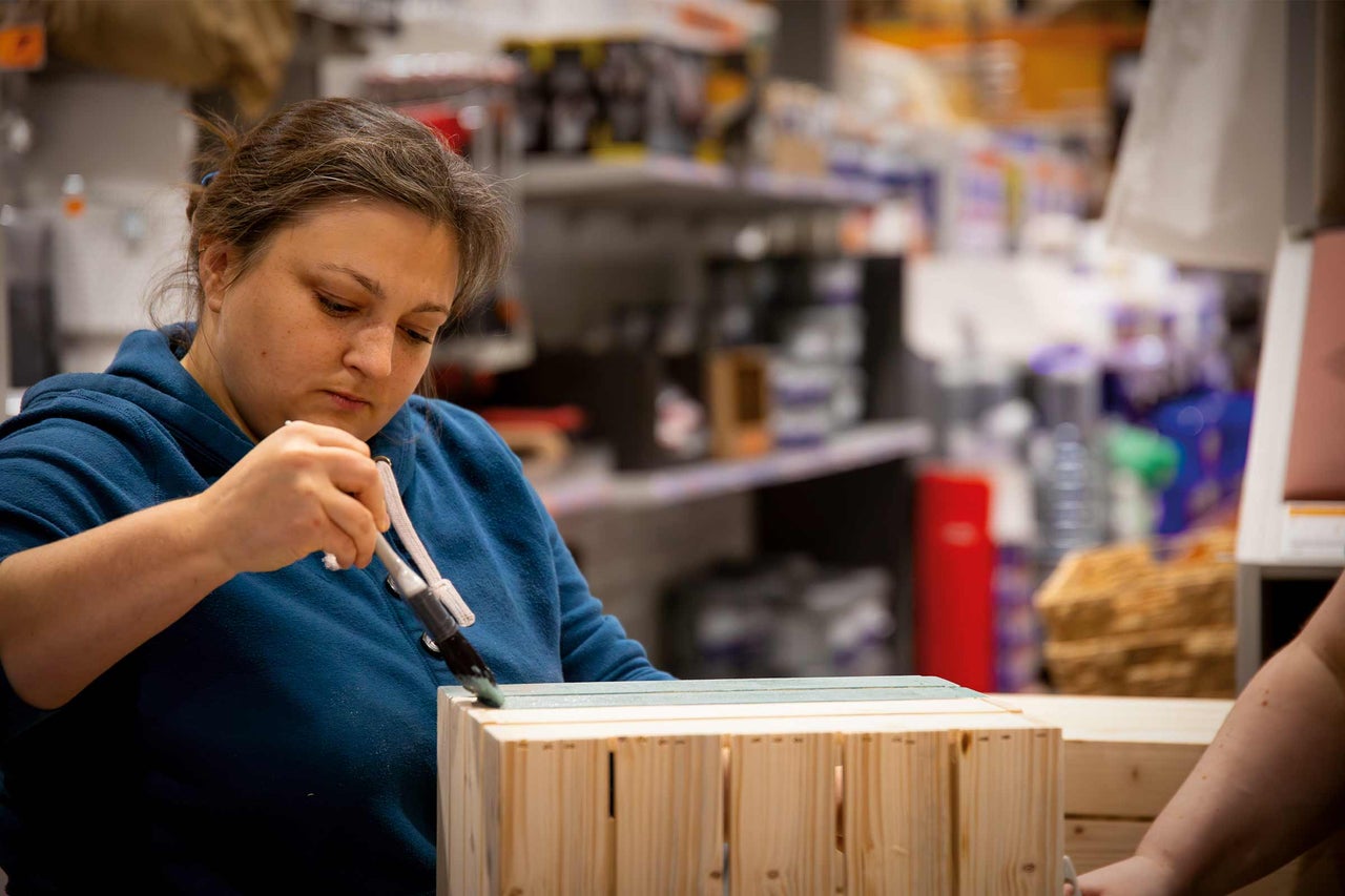 Femme peint une caisse en bois avec un pinceau