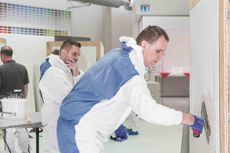 Des personnes portent des vêtements de protection et appliquent du plâtre sur un mur.