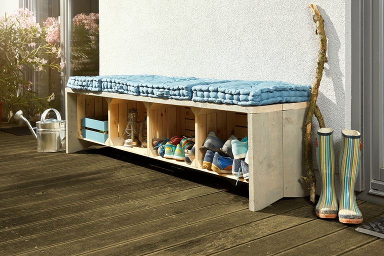 Banc de vestiaire en caisses en bois avec étagère à chaussures et coussin d'assise sur une terrasse avec arrosoir et bottes en caoutchouc