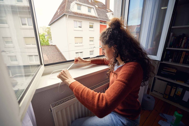 Frau befestigt Dichtungsband an einem Fensterrahmen für die Fensterabdichtung