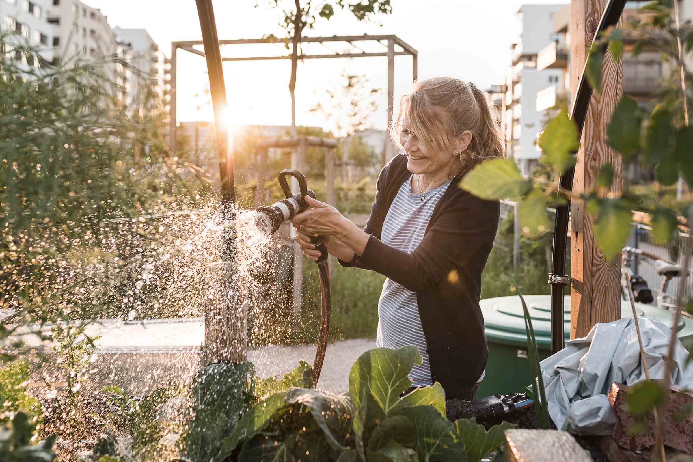 Femme arrose les plantes avec un tuyau d'arrosage dans le jardin.