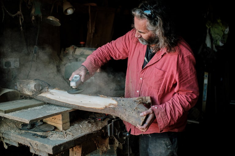 Un homme ponce un morceau de bois avec une ponceuse dans un atelier.