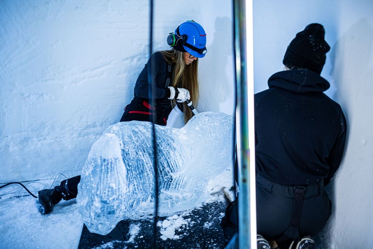 Sculpteur sur glace travaillant sur une sculpture de glace avec des outils et des vêtements de protection.